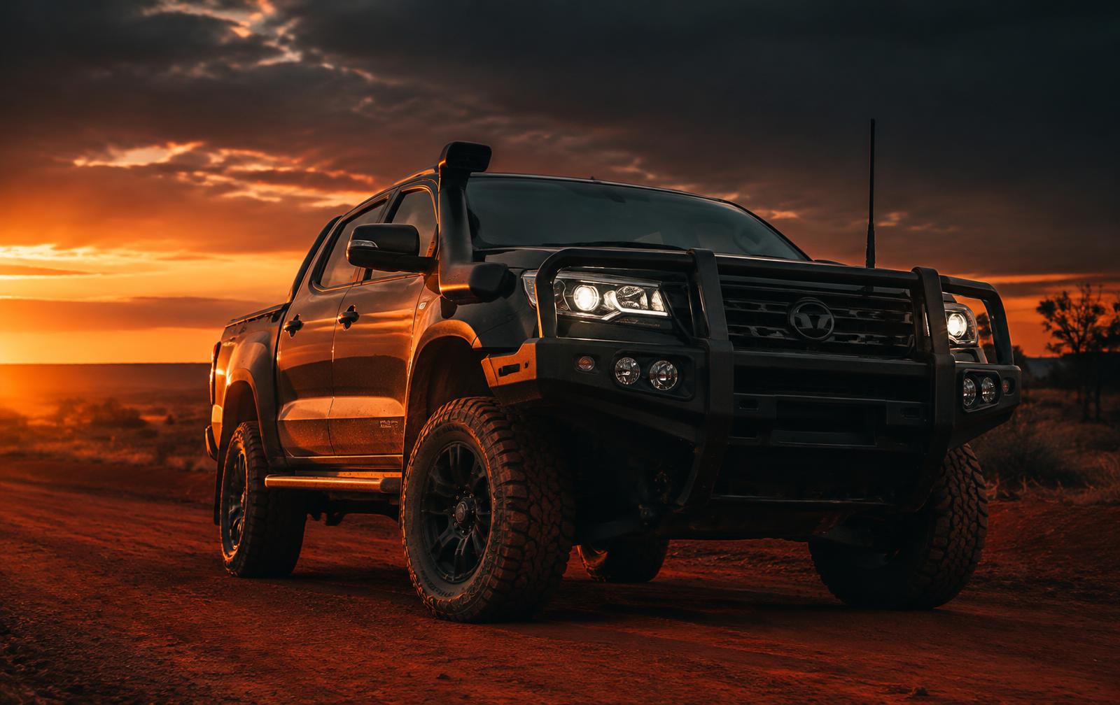 Dark 4WD ute with bull bar and snorkel on an outback track at dusk
